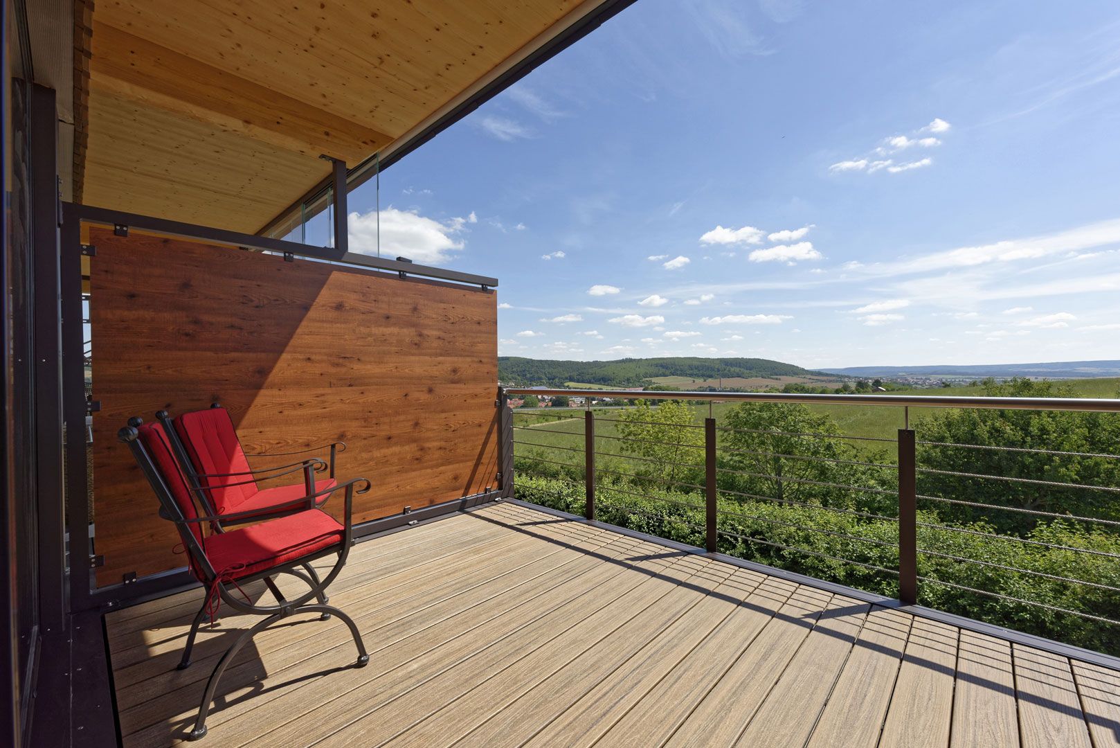 Stilvolle WPC Terrasse auf einem Balkon mit rotem Stuhl und toller Aussicht.