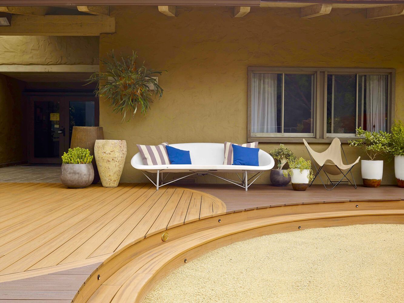Teilüberdachte und rund ausgeführte Terrasse mit Pflanzenkübeln und Sitzgelegenheit.