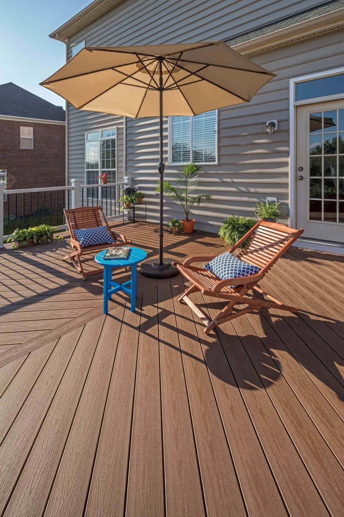 Vornehme Terrasse mit Sonnenschirm und Stühlen vor einem Landhaus.